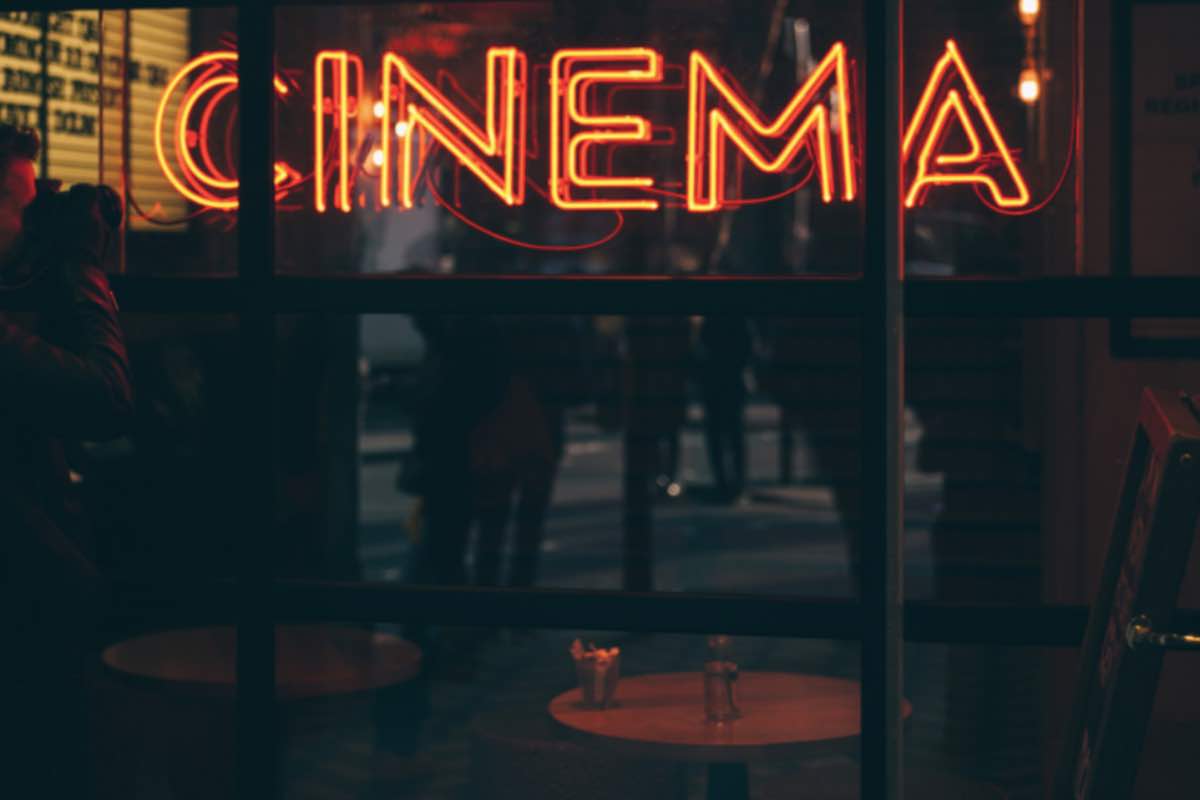 Uomo fotografa la vetrata di un locale con insegna a neon di un cinema